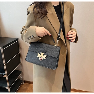 Detailansicht einer schwarzen Lederhandtasche mit goldener Bienenschließe und Perlen