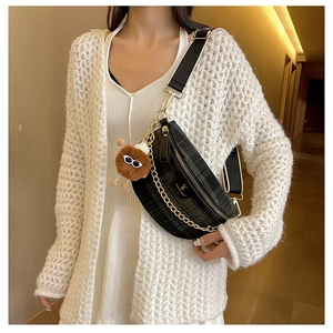 Detail of black quilted crossbody bag with golden chain and funny plush ball charm