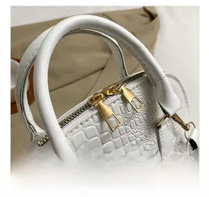 Close-up of white crocodile pattern handbag featuring gold dual zippers and smooth handles