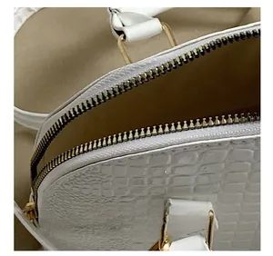 Close-up of golden zipper hardware and crocodile embossed texture on a white handbag