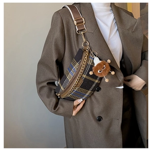 Detail view of plaid crossbody chest bag with golden chain and plush keychain accessory