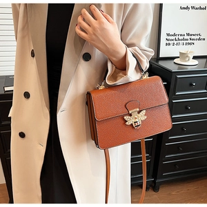 Detail einer orangefarbenen Ledertasche mit perlbestetztem Bienen-Metallverschluss