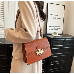 Braune Leder-Handtasche mit goldener Bienenschließe und Perlen-Detail an einem Modell