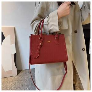 Close-up of red quilted leather tote bag featuring gold lettering and heart charm