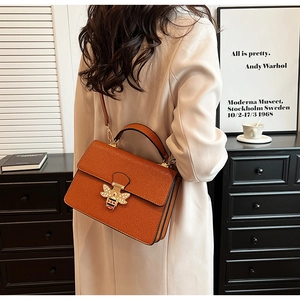 Detail der goldenen Bienenschließe mit Perlen und Kristallen auf orangefarbener Ledertasche