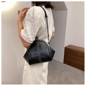 Detail of black cross-stitched kiss-lock bag with chain strap worn by a model