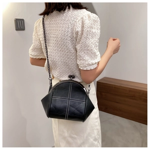 Detail of black shell-shaped crossbody bag featuring white cross-stitch and chain strap