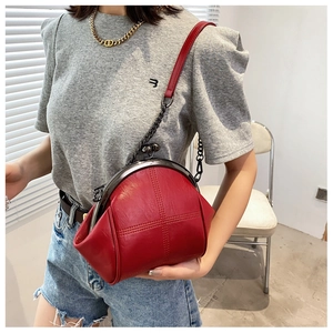 Detail of red shell-shaped bag with vintage clasp and leather chain strap shown on model