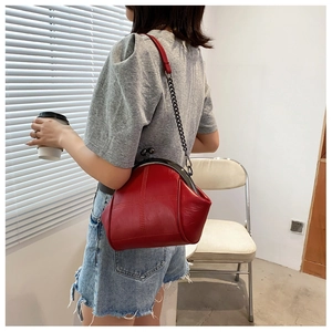 Detail of red vintage leather shell bag featuring cross stitching and metal chain strap