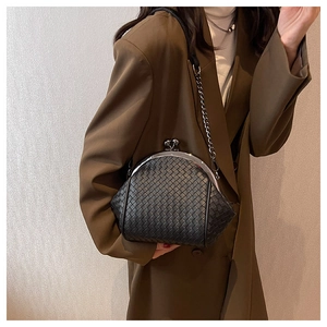 Detail of a black woven shell bag with metal chain strap worn with a blazer