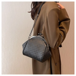 Detail of black woven shell bag with metallic ball clasp and chain strap on wool coat