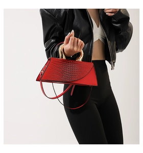 Detail of red crocodile pattern handbag with round gold handle and leather strap