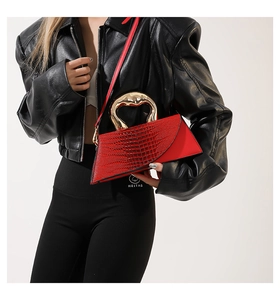 Macro view of red crocodile-embossed handbag featuring a gold metallic curved handle