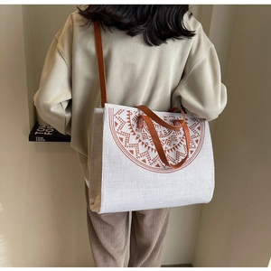 Detail of canvas tote bag showing brown geometric print and leather handle on a model