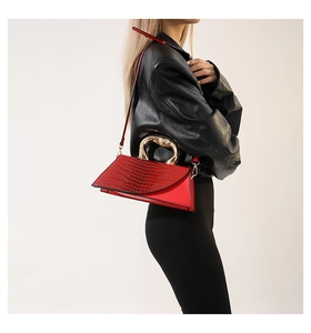 Detail of red crocodile pattern handbag with gold curved handle shown on a model