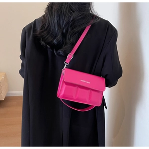 Detail of vibrant magenta crossbody bag with rectangular embossing and white text