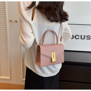 Detailed view of dust pink rectangular handbag with gold metal bar hardware worn on shoulder