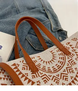 Detail of woven tote bag with brown leather handles and reinforced cross stitching