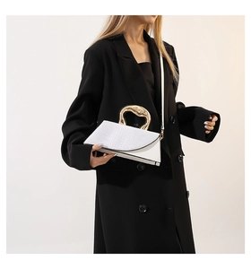 White crocodile pattern handbag with unique gold metal handle on a black suit blazer