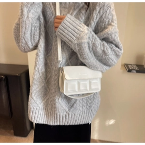 Detail of white rectangular crossbody bag featuring textured square embossing and flap closure