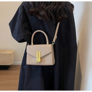 Beige retro crossbody bag with gold metal buckle shown on model in a minimalist setting