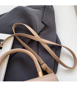Detail of beige litchi leather bag with adjustable gold buckle and smooth shoulder strap