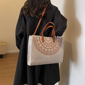 Large beige canvas tote bag with brown geometric prints and leather handles on a model