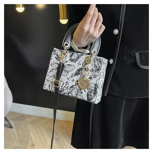 Close-up of black and white floral embroidery on a handbag with golden heart charm