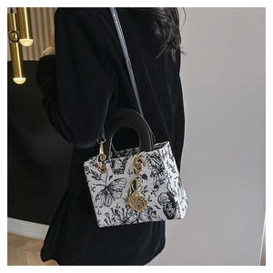 Detail of embroidered tote bag featuring butterfly patterns and gold heart pendant