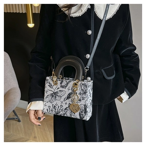 Detail of butterfly embroidered pattern and gold heart pendant on handbag