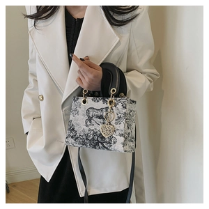 Detail of embroidered tiger landscape bag with dual leather handles and gold heart charm