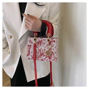 Detail of floral embroidery and heart pendant on a white shoulder bag with red straps