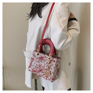 Detailed embroidery of red flowers and butterflies with a gold heart charm on handbag