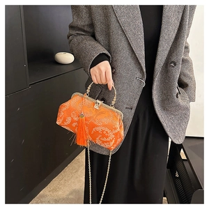 Detail of bright orange jacquard handbag with floral patterns, tassel and metal chain