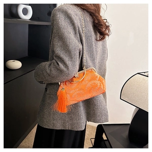 Detail of embroidered floral pattern on orange shell bag with silk tassels and gold chain