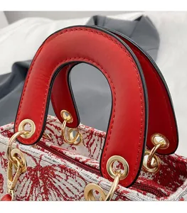 Detail of red leather handles and gold metal hardware on embroidered tote bag