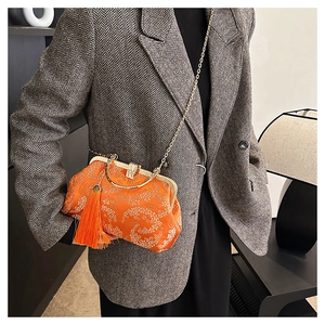 Détail du sac en soie orange avec broderie florale, pompon et bandoulière dorée