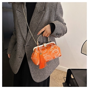 Detail of vibrant orange Chinese style embroidery handbag with tassel and gold chain strap