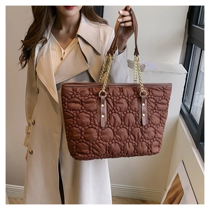 Borsa tote trapuntata marrone con catena dorata indossata da modella in trench beige