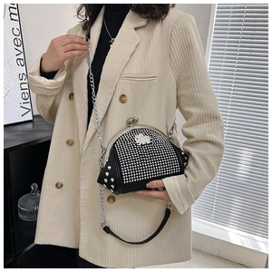 Detail of a black shell bag with silver rhinestones and metal chain on a beige blazer