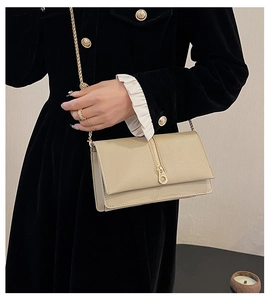 Detail of beige cross-grain leather bag with gold chain strap on black dress