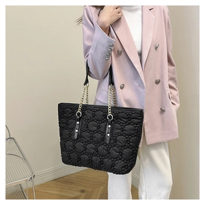 Borsa tote trapuntata nera con catena dorata indossata da modella con blazer rosa