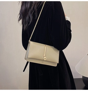 Detail of light khaki chain bag with pebbled texture and gold zipper ring on a black dress
