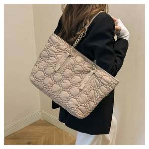 Dettaglio della borsa tote trapuntata beige con catena dorata indossata dalla modella