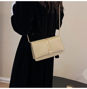 Detail of beige textured leather crossbody bag with gold chain strap worn by a model