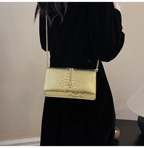 Detail of gold chain strap on a metallic textured shoulder bag over a black dress