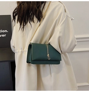 Detail of dark green leather shoulder bag with gold chain and vertical zipper accents
