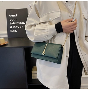Close-up of a dark green leather crossbody bag with gold chain and large ring zipper