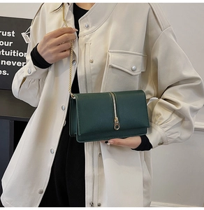 Close-up of a dark green leather crossbody bag featuring a golden vertical zipper and chain