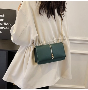 Detail of a dark green chain strap bag with gold zipper accent on textured leather